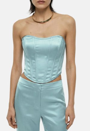Donna che indossa un top corsetto senza spalline in raso azzurro chiaro e pantaloni a vita alta abbinati con una collana choker dorata.