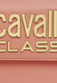 Bolso de mano de cuero rosa con un destacado logo dorado en la parte frontal. Textura suave con detalles de costura y una forma estructurada.