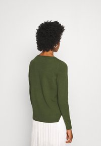 Mörkgrön tröja med långa ärmar, rundad halsringning och ribbad nederkant. Tyget verkar mjukt och texturerat.