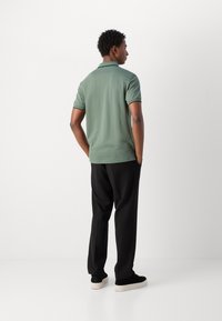 Groene polo met zwarte kraag en boorden, gecombineerd met zwarte broek en zwarte sneakers. Gladde stof, relaxte pasvorm.