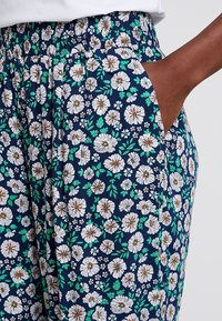 Spodnie w kwiatowy nadruk z granatowym tłem, białymi kwiatami i zielonymi liśćmi, elastycznym paskiem w talii oraz bocznymi kieszeniami.