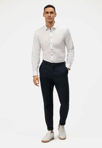 Witte lange mouwen shirt met donkere knopen, gecombineerd met marineblauwe broek en witte sneakers. Schoon ontwerp met een getailleerde silhouet.
