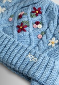 Mėlyna megzta kepurė su kabelių raštu ir išsiuvinėtomis gėlėmis raudona, rožine ir balta spalvomis. Gofruota kraštinė su „jojo“ balta siūle.