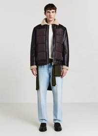 Veste en cuir brun et matelassée avec un col en shearling beige, portée par-dessus un pull en tricot blanc, associée à un jean droit bleu clair.
