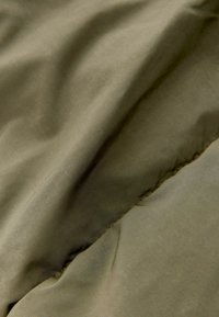 Tissu olive vert doux avec un subtil éclat, présentant une texture lisse et de légères rides, mettant en valeur des coutures le long d'un bord.