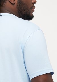 Light blue cotton t-shirt with short sleeves, round neckline, and smooth texture. Visible stitching on the sleeve. Simple and casual design.
