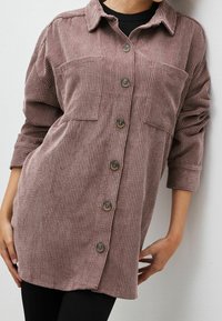 Camisa de botones en una tela texturizada y acanalada, de un suave color malva, con dos bolsillos en el pecho y mangas largas con puños doblados.