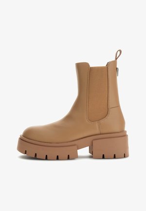 Botte de cheville en cuir tan avec des panneaux élastiques sur les côtés, semelle épaisse et tirette au talon. Texture lisse et construction solide.