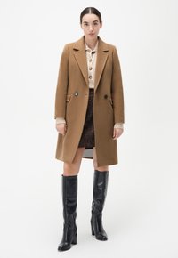 Bruine wollen jas met een dubbelgeknoopte stijl, met notch lapels en twee voorzakken, gelaagd over een licht crèmekleurig topje en een bedrukte rok.