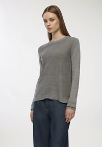 Szary sweter z dzianiny z długimi rękawami, okrągłym dekoltem i prążkowanym wykończeniem; noszony z niebieskimi dżinsami. Delikatna tekstura na całym ubraniu.