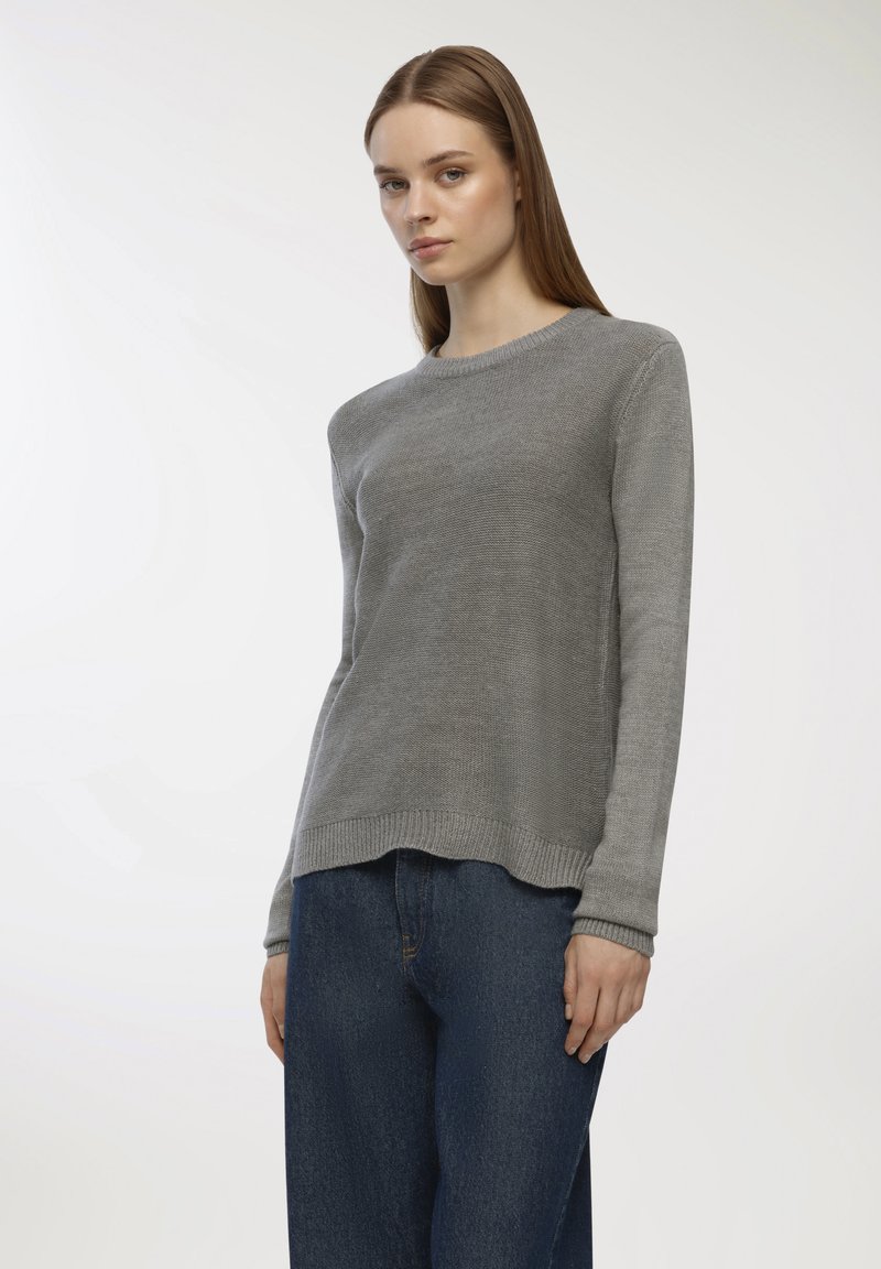 Szary sweter z dzianiny z długimi rękawami, okrągłym dekoltem i prążkowanym wykończeniem; noszony z niebieskimi dżinsami. Delikatna tekstura na całym ubraniu.