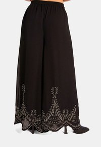 Pantaloni neri a gamba larga con vita elastica, caratterizzati da un intricato ricamo argento sull'orlo e una consistenza leggera e fluida.