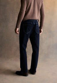 Jeanși dark blue din denim, cu un design drept, două buzunare pe spate și cusături contrastante pe un fundal texturat.