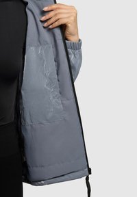 Pilkas pūkinis švarkas su vidine kišene, turintis lygų paviršių, elastines rankogalius ir užtrauktuką priekyje.