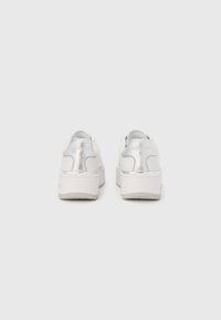 Valged platvorm-tennised metallikdetailidega, ümmargune nina, sile nahkpind ja iseloomulik tagumine paneelilogo.