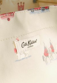 Produs Cath Kidston cu o țesătură albă și modele colorate de cai, trăsuri și coroane. Etichetă cusută la margine.