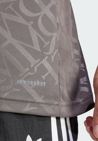 Maglietta sportiva grigia con trama e tessuto a rete, caratterizzata da un motivo sottile e il logo "AEROREADY" in grigio chiaro vicino all'orlo.