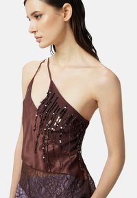 Top in satin di un profondo viola decorato con paillettes nere che cadono verticalmente, caratterizzato da un design a spalla unica con un orlo in pizzo nella parte inferiore.