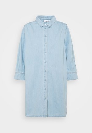 Chemise en denim bleu clair avec un col pointu, fermeture à boutons et manches trois-quarts, présentant une coupe décontractée et des détails de couture minimalistes.