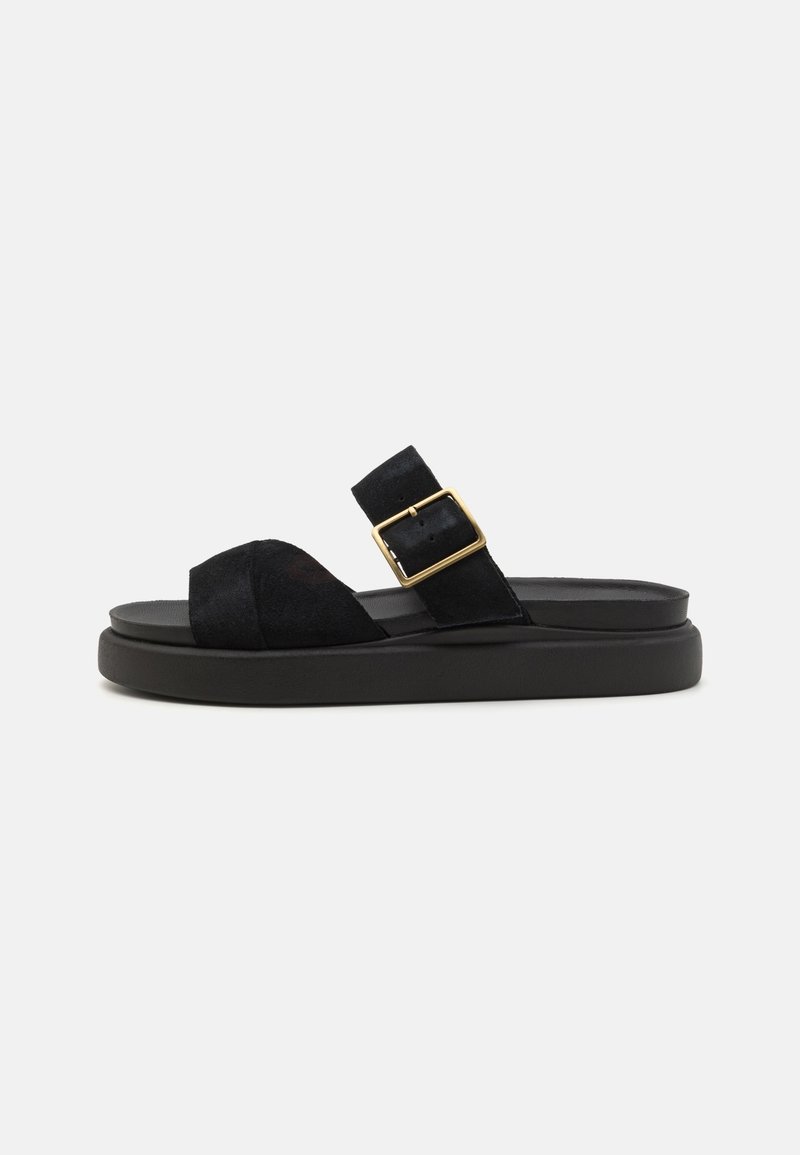 Sandales glissantes en daim noir avec une grande bride supérieure et une boucle carrée dorée en accent. Elles présentent une semelle noire épaisse et un design à bout ouvert.