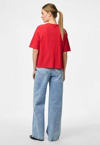 Crvena pamučna oversized majica s kratkim rukavima, u kombinaciji s svijetloplavim širokim trapericama. Jednostavan dizajn bez vidljivih uzoraka ili naglasaka.