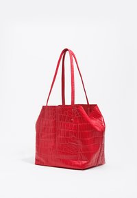 Rdeča torba tote iz usnja z teksturo krokodilje kože, z dvema dolgima ročajema, pravokotnim dnom in vidnim šivom na belem ozadju.