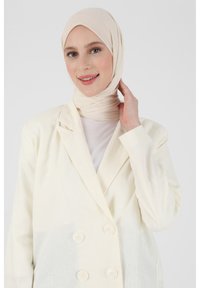 Cream double-breasted blazer in lightweight fabric, featuring a lapel collar and textured surface, paired with a matching light beige scarf.