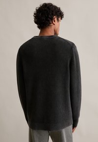 Tmavý žebrovaný svetr s kulatým výstřihem a dlouhými rukávy, se strukturovaným povrchem. Pletený materiál s jemnými variacemi v odstínu.