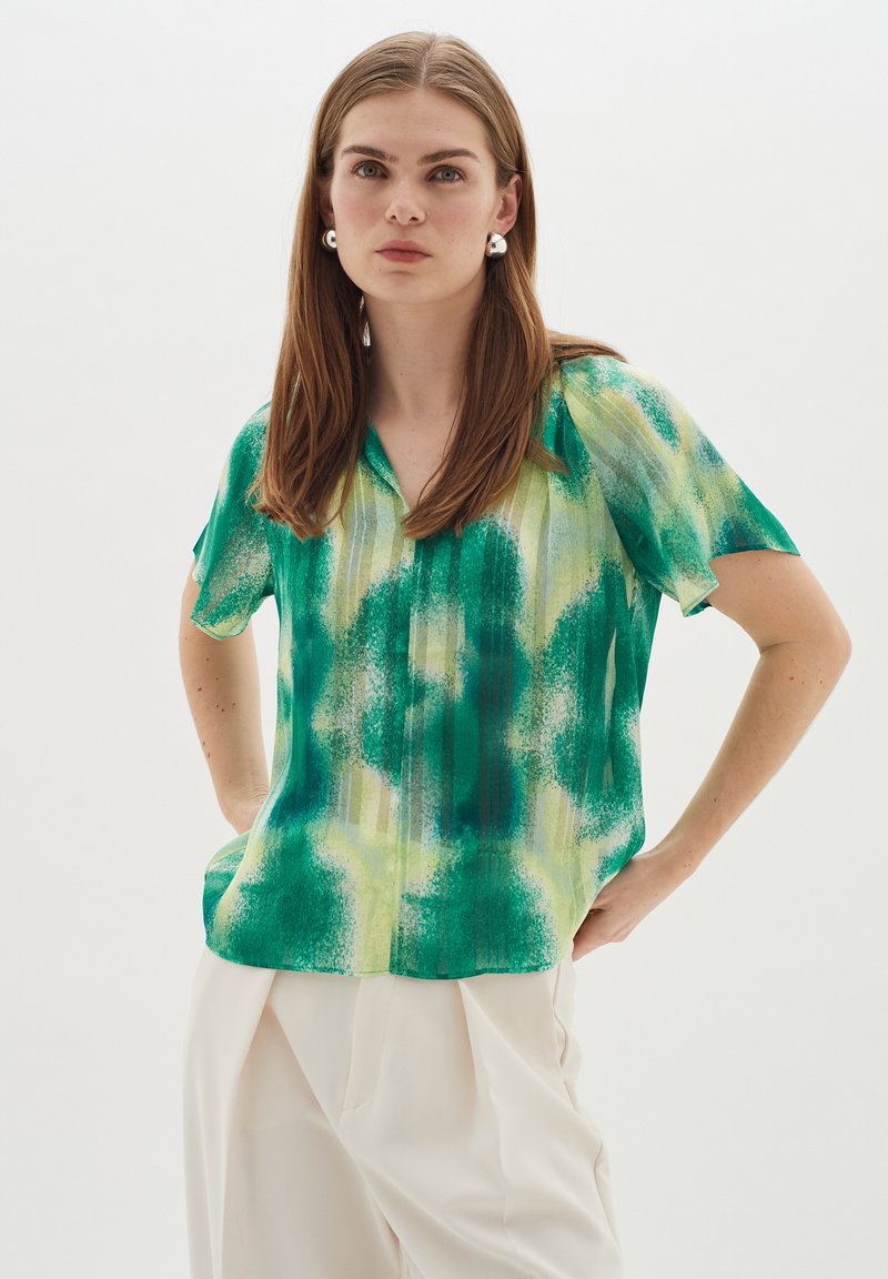 Blusa a maniche corte, con scollo a V, in un motivo astratto verde e giallo, realizzata in un tessuto leggero con una texture liscia e una vestibilità rilassata.