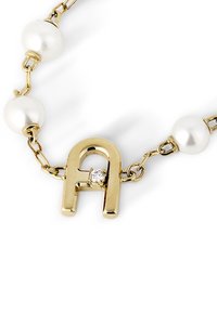 Zelta ķēdes aproce ar baltām pērļām un zelta pakavs formas piekariņu ar nelielu caurspīdīgu dārgakmeni.