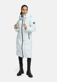 Light blue puffer coat with a hood, vertical stitching, two zippered pockets, and black accents. Worn over black pants and chunky black boots.