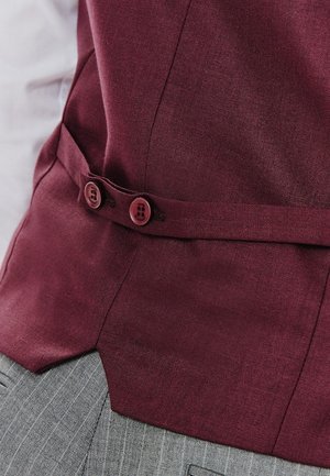 Burgundowa bluzka z teksturowanej tkaniny, z dwoma okrągłymi guzikami w talii, połączona z jasnoszarym materiałem w paski poniżej.