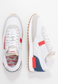 Bílo-šedé síťované tenisky s červenými a modrými akcenty, gumovou podrážkou a polstrovaným jazykem s logem. Texturované detaily z broušené kůže a gumy.