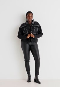 Black denim jacket featuring silver studs, button closure, and two front pockets. Paired with slim black leather pants and ankle boots.