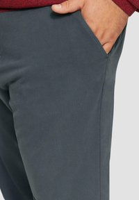 Grijze katoenen broeken met een gladde textuur, zijzakken en netjes gestikte naden. De stof lijkt duurzaam en flexibel te zijn.