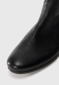 Close-up of black leather ankle boot with rounded toe and smooth texture on white background.