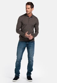 Bruin poloshirt met lange mouwen en kraag, slim-fit, gecombineerd met blauwe strakke jeans en zwarte suède sneakers. Eenvoudig en modern design.