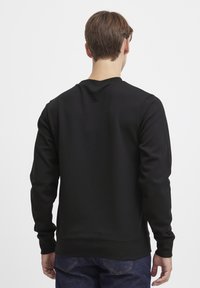 Black sweatshirt featuring a crew neck, ribbed cuffs, and smooth texture, paired with dark blue jeans. Focus on minimalist design.