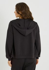 Sweat à capuche noir surdimensionné avec capuche à cordon, coupe décontractée et poignets côtelés. Tissu lisse et doux sans motifs visibles.