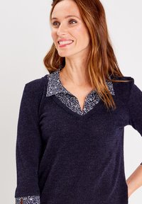 Marineblaues Strickoberteil mit V-Ausschnitt und Dreiviertelärmeln. Hat einen kontrastierenden Kragen mit floralem Muster. Weicher Stoff, lässiges Design.
