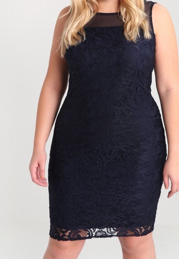 Femme portant une robe en dentelle noire ajustée sans manches, avec un panneau transparent au niveau du décolleté et des détails floraux en dentelle.