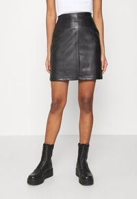Schwarzer Leder-Minirock mit hoher Taille, ausgestattet mit Frontnähten und Seitentaschen, kombiniert mit schwarzen Schnürankle boots.