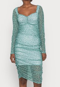Robe en teal à manches longues avec une silhouette ajustée, présentant un design froncé et un motif floral avec de subtils accents blancs.