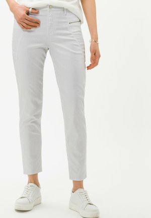 Pantalones ajustados de color gris claro con un sutil patrón de rayas verticales, que cuentan con un bolsillo con cremallera y una longitud de tobillo recortada. Combinados con zapatillas blancas.