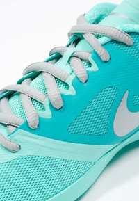 Turkusowy but sportowy z siateczkową cholewką, teksturowanymi akcentami i szarymi sznurowadłami. Zawiera wyraźne logo po boku.