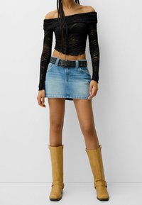 Černý top odhalený na ramena s texturovaným vzorem, denimová minisukně, černý pásek s nýty a hnědé kozačky ke kolenům se sponami.