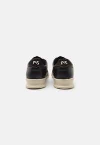 Zapatillas negras con parte superior de cuero liso, suela de goma beige y logo blanco "PS" en la parte trasera. Forma redondeada con cuello acolchado.