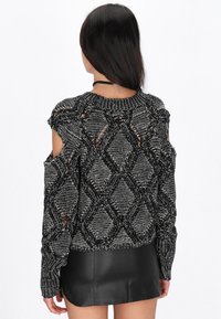 Maglione lavorato a maglia in bianco e nero con motivi a rombi, spalle scoperte e colletto a coste, abbinato a una mini gonna in pelle nera.