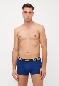 Boxers azul de algodón, con una cinturilla elástica negra que lleva el logo "LACOSTE". Diseñados en un estilo ajustado. Textura suave.
