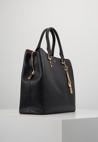 Borsa a mano in pelle nera con finitura testurizzata, hardware dorato, chiusura con zip laterale e una catena decorativa con lucchetto.